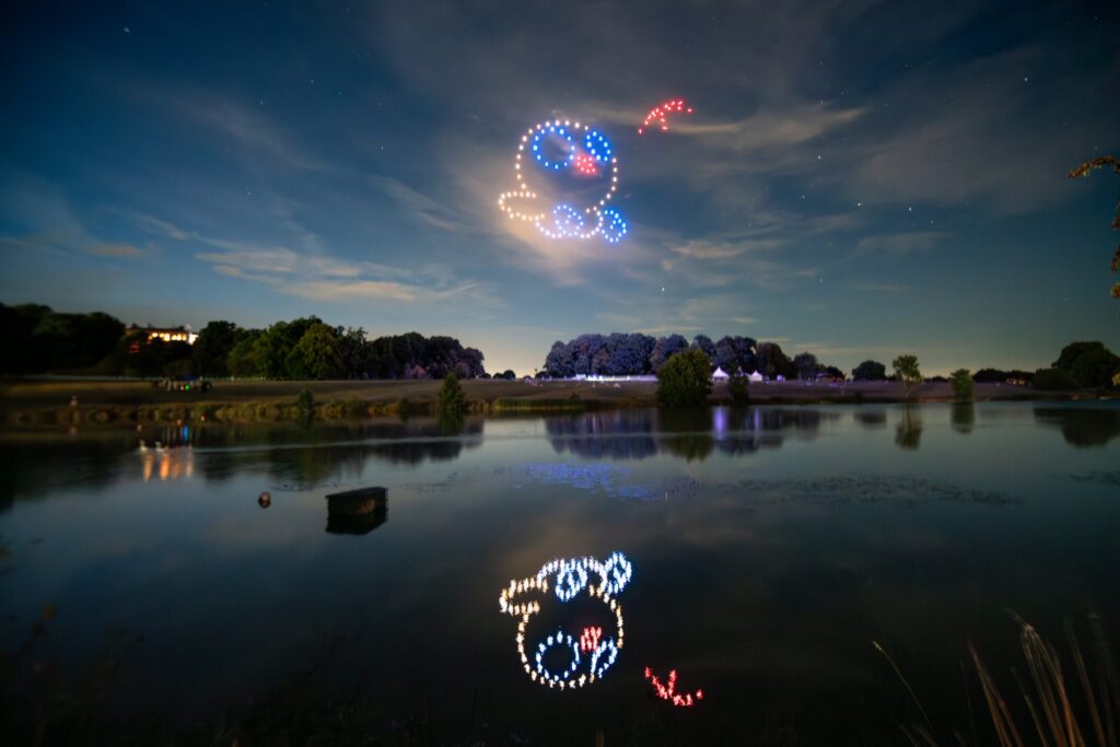 A dazzling drone light show forms a character over a serene night lake, reflecting beautifully on the water's surface.