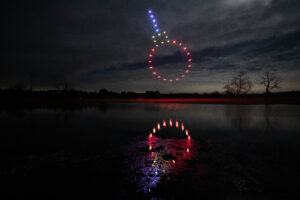 A circle of drones illuminates the night sky, reflected in a serene body of water below.