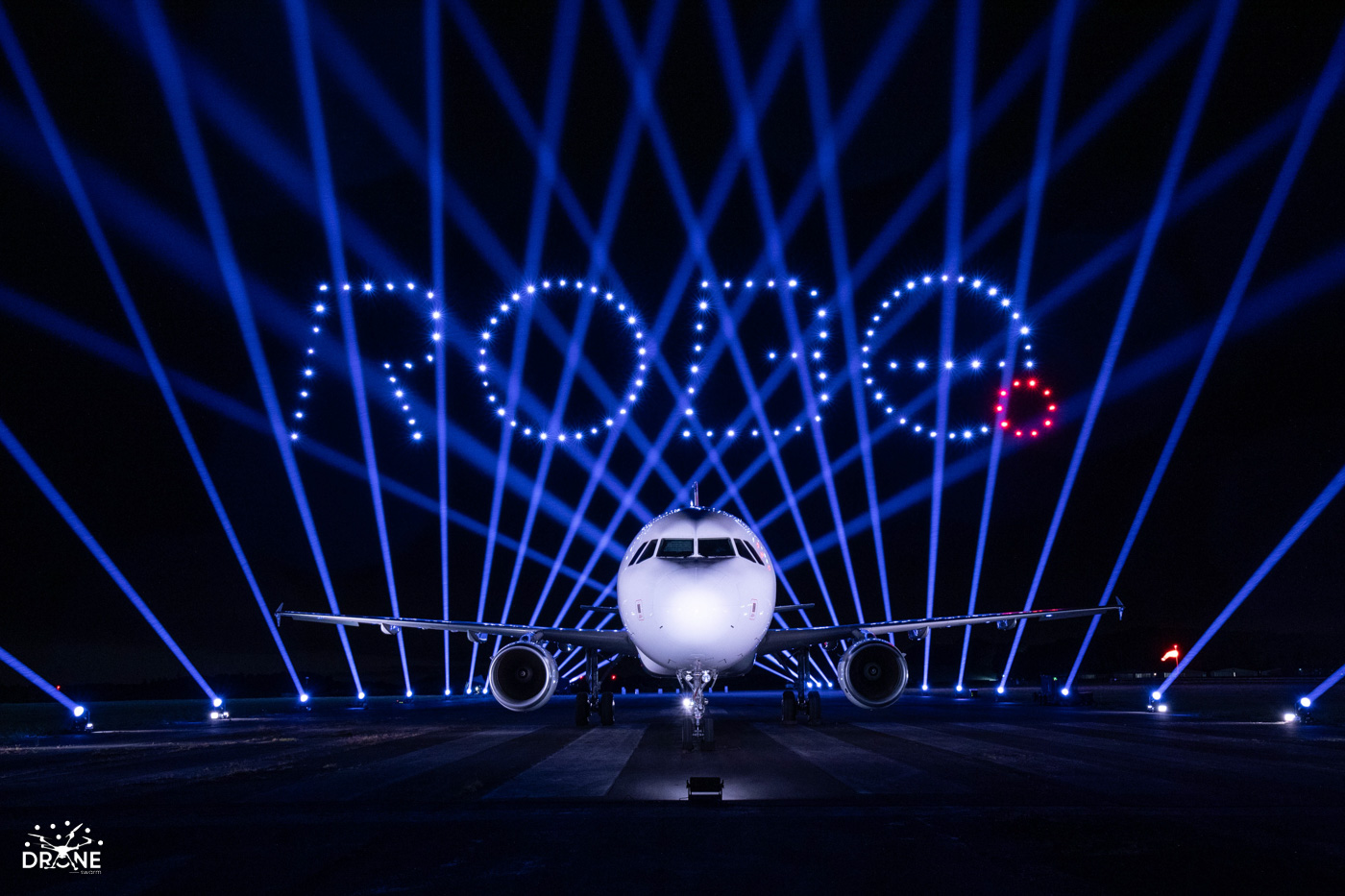 Airplane on runway at night with bright lights spelling "ROSE" in the sky.