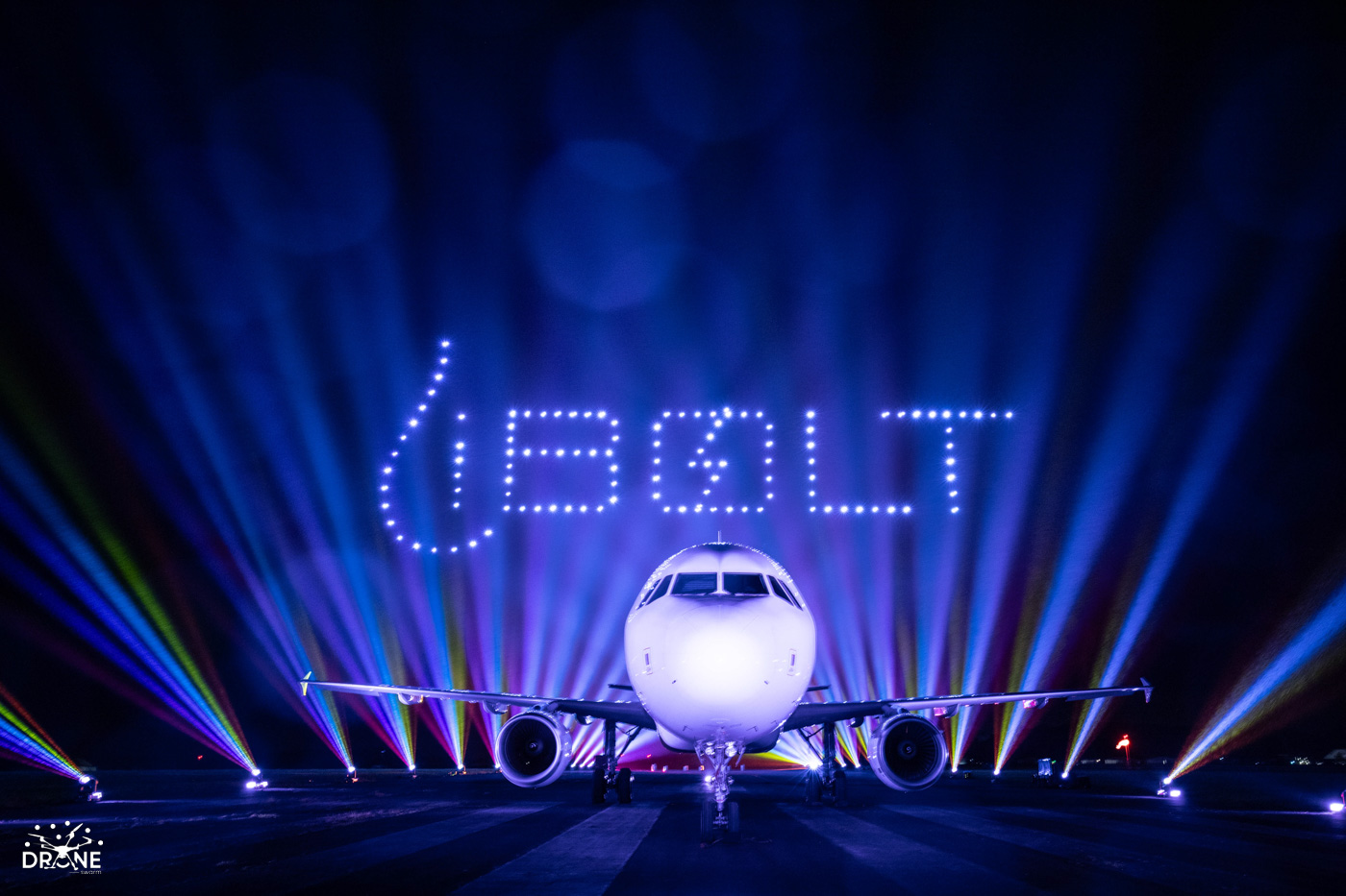 An airplane with colorful lights and "BOLT" spelled above in glowing letters at night.