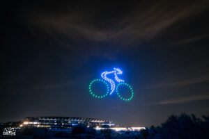 Drones form a bicycle and rider in the night sky above a stadium.