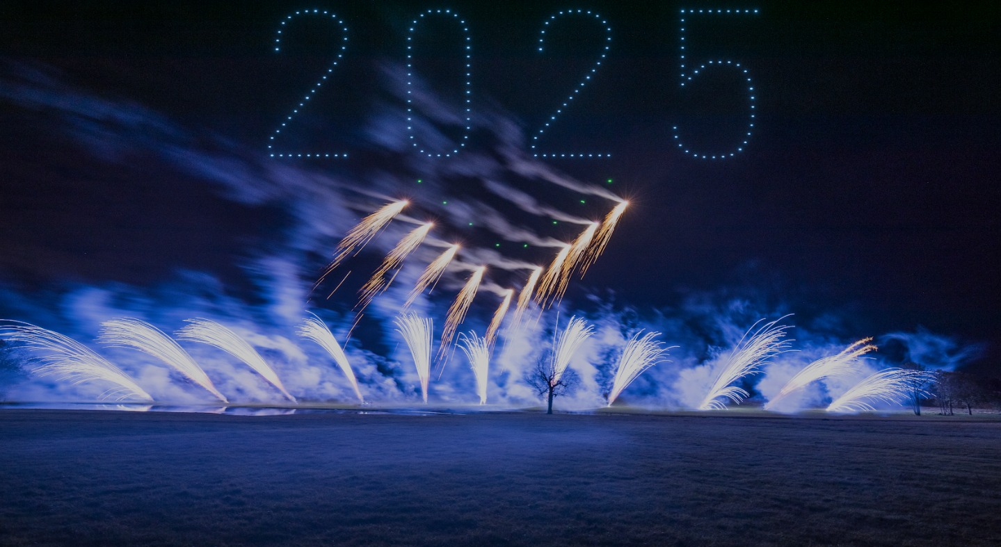 Drones form "2025" in the night sky with fireworks below against a dark background.